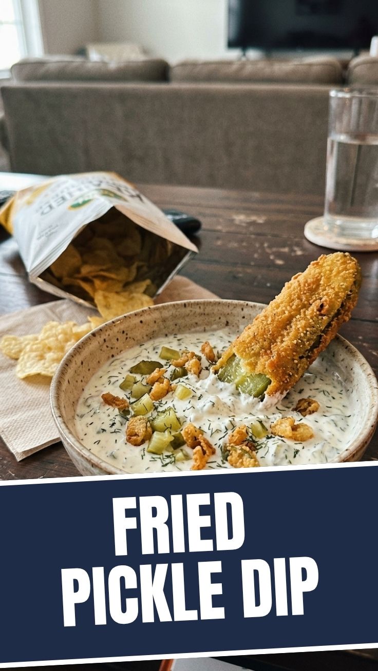 A bowl of creamy fried pickle dip, garnished with fresh dill and fried pickle pieces.